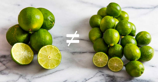 Vergleich von echten Limetten (Key Limes) und gewöhnlichen Limetten auf einer Marmorplatte. In der Mitte zeigt ein Symbol ≠ den Unterschied zwischen beiden.