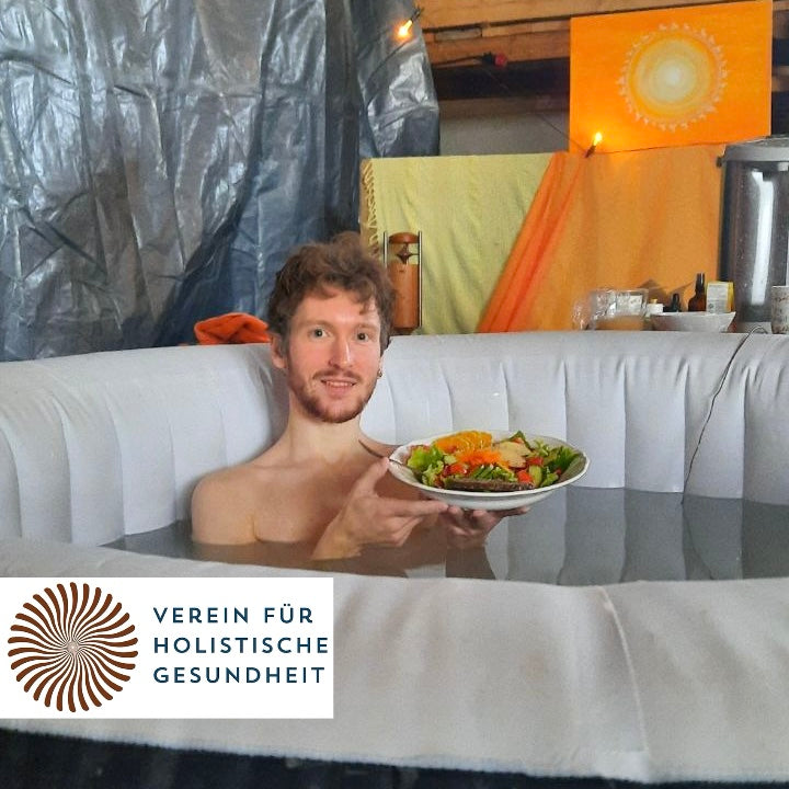 Maxi sitzt in einem aufblasbaren Badepool und hält einen Teller mit frischem Salat. Er nimmt am Langzeit Basenbaden teil, um Körper und Geist zu revitalisieren. Unten im Bild ist das Logo des Vereins für Holistische Gesundheit zu sehen.